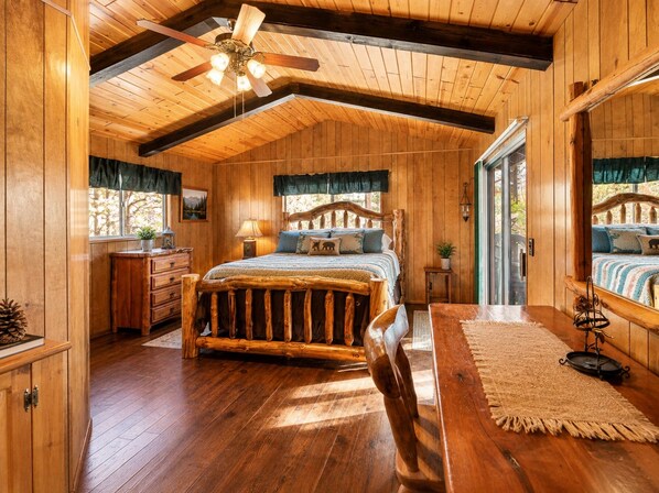 A wooden cabin bedroom with a bed, dresser, and a ceiling fan.