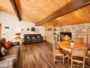 A cozy living room with a fireplace, wooden furniture, and a stone accent wall. - Moonridge Manor - Close to Slopes, Hot Tub, Game Room, Pool Table (Big Bear Lake)