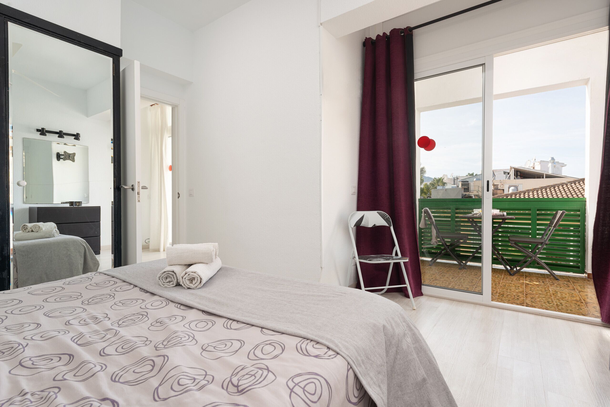 Ein Schlafzimmer mit Bett, Spiegel, Sessel und Blick ins Freie.
