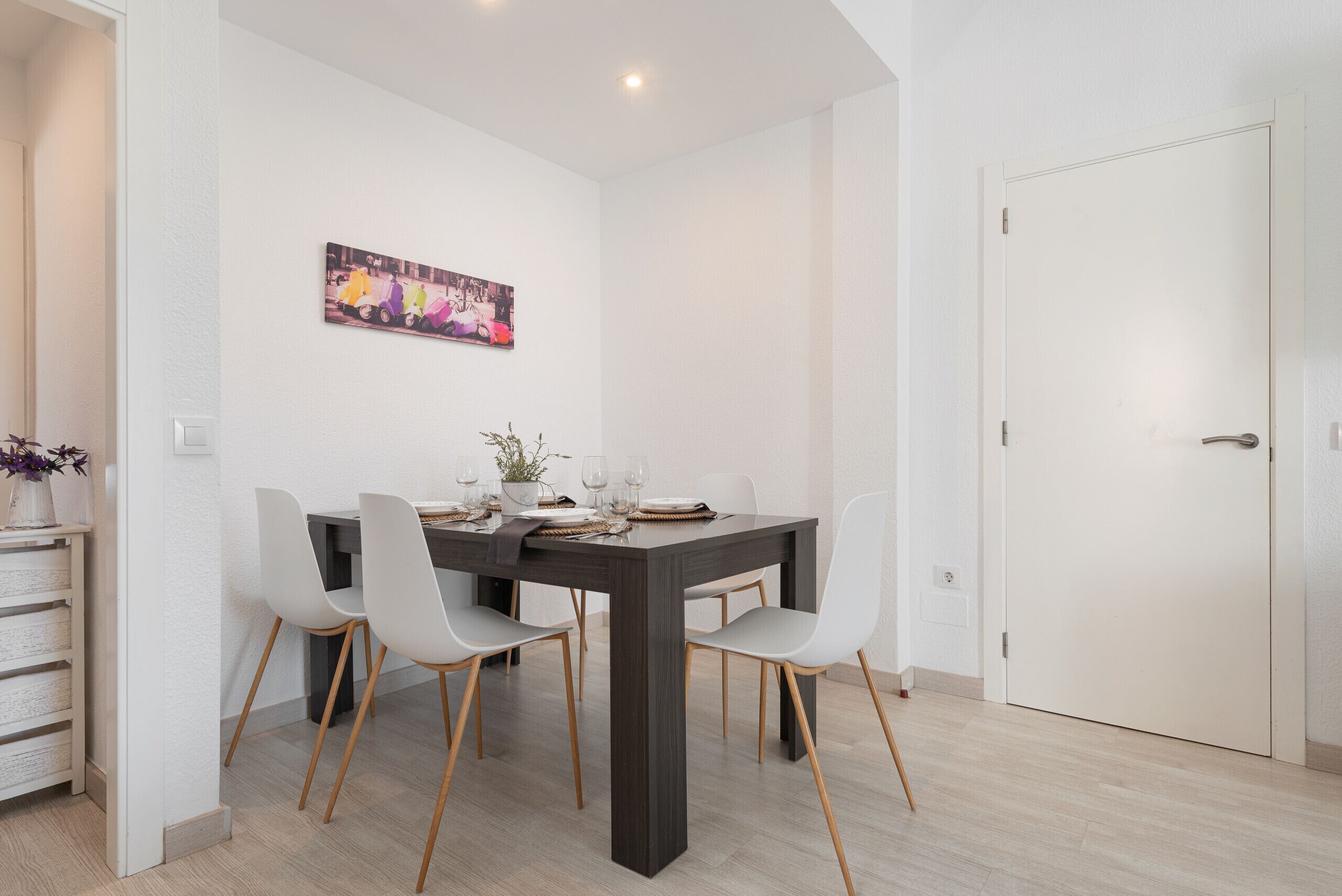 Un comedor con una mesa de madera oscura, sillas blancas y un cuadro colorido en la pared.
