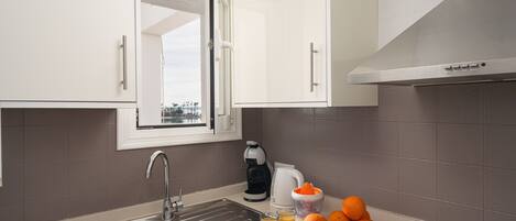 A modern kitchen with a stainless steel sink, a coffee maker, a kettle, and a cutting board with oranges.