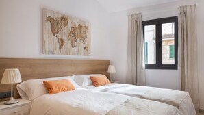Ein Doppelbett mit weißer und orangefarbener Bettwäsche, ein Holz-Kopfteil, eine Weltkarte als Wandbild, ein Nachttisch mit Lampe und ein Fenster mit Vorhängen.