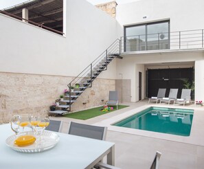 Un área de piscina moderna al aire libre con barandilla de vidrio, una escalera que lleva a un nivel superior y una zona de estar con sillones reclinables.