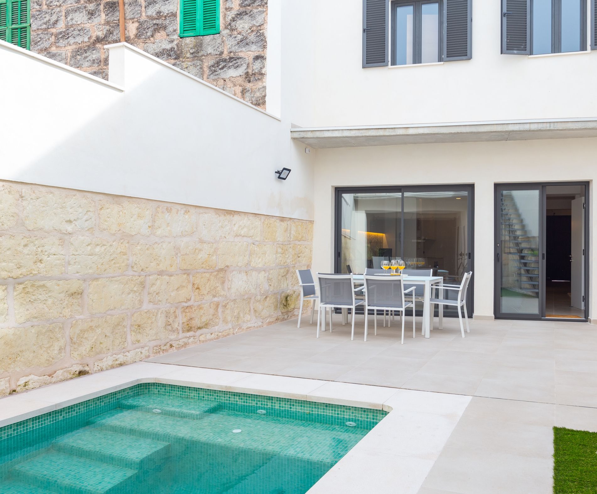 Une maison moderne dotée d’une piscine, d’un coin repas avec mobilier d’extérieur et d’un mur en pierre.