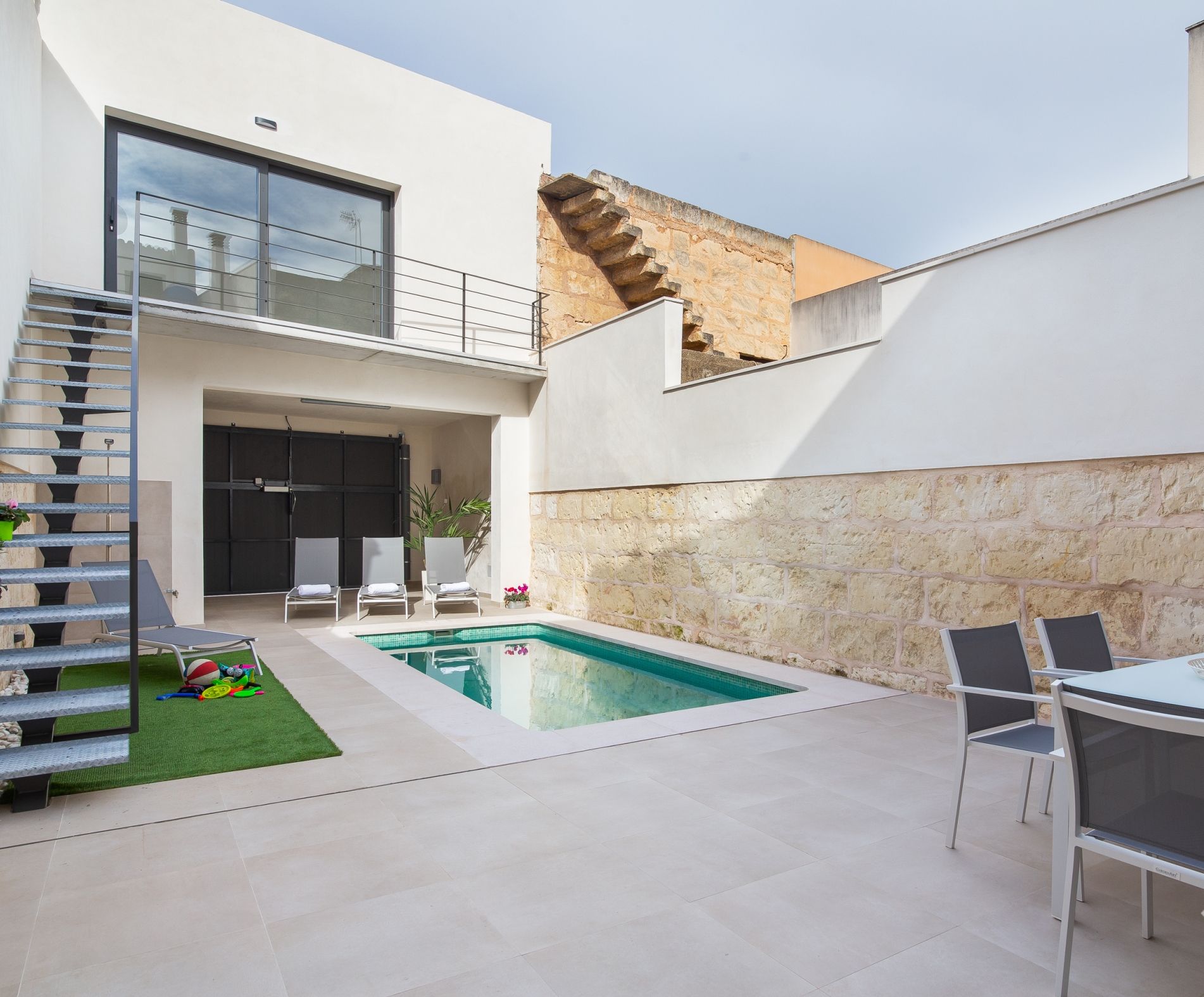 Un espace de vie extérieur moderne doté d’une piscine, d’un coin salon abrité et d’un escalier menant à un balcon.