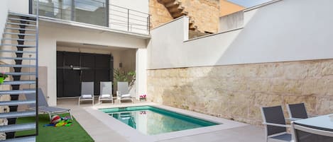 Un espace de vie extérieur moderne doté d’une piscine, d’un coin salon abrité et d’un escalier menant à un balcon.