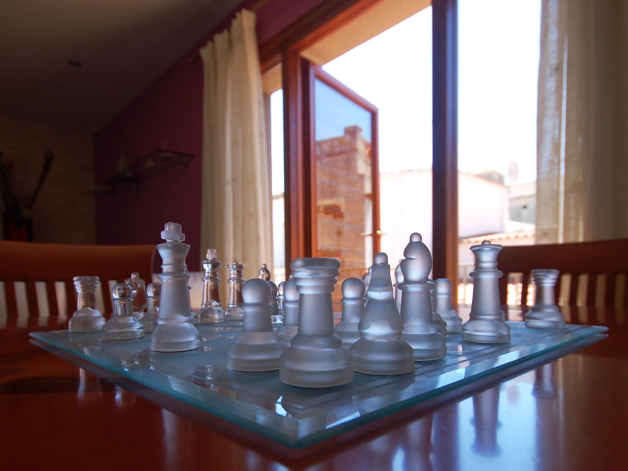 Un tablero de ajedrez sobre una mesa de vidrio, con vista a un edificio a través de una ventana.