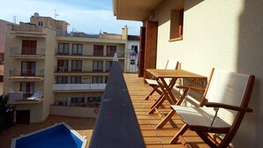 A balcony with a pool, wooden furniture, and a view of neighboring buildings. - CENTRIC APARTMENT with POOL in TOSSA (Tossa de Mar)
