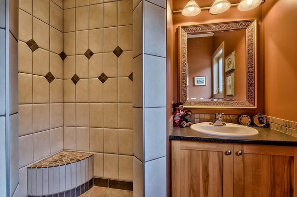 Un baño con zona de ducha con un estampado geométrico de azulejos, un lavamanos con mueble de madera y un espejo con marco decorativo.