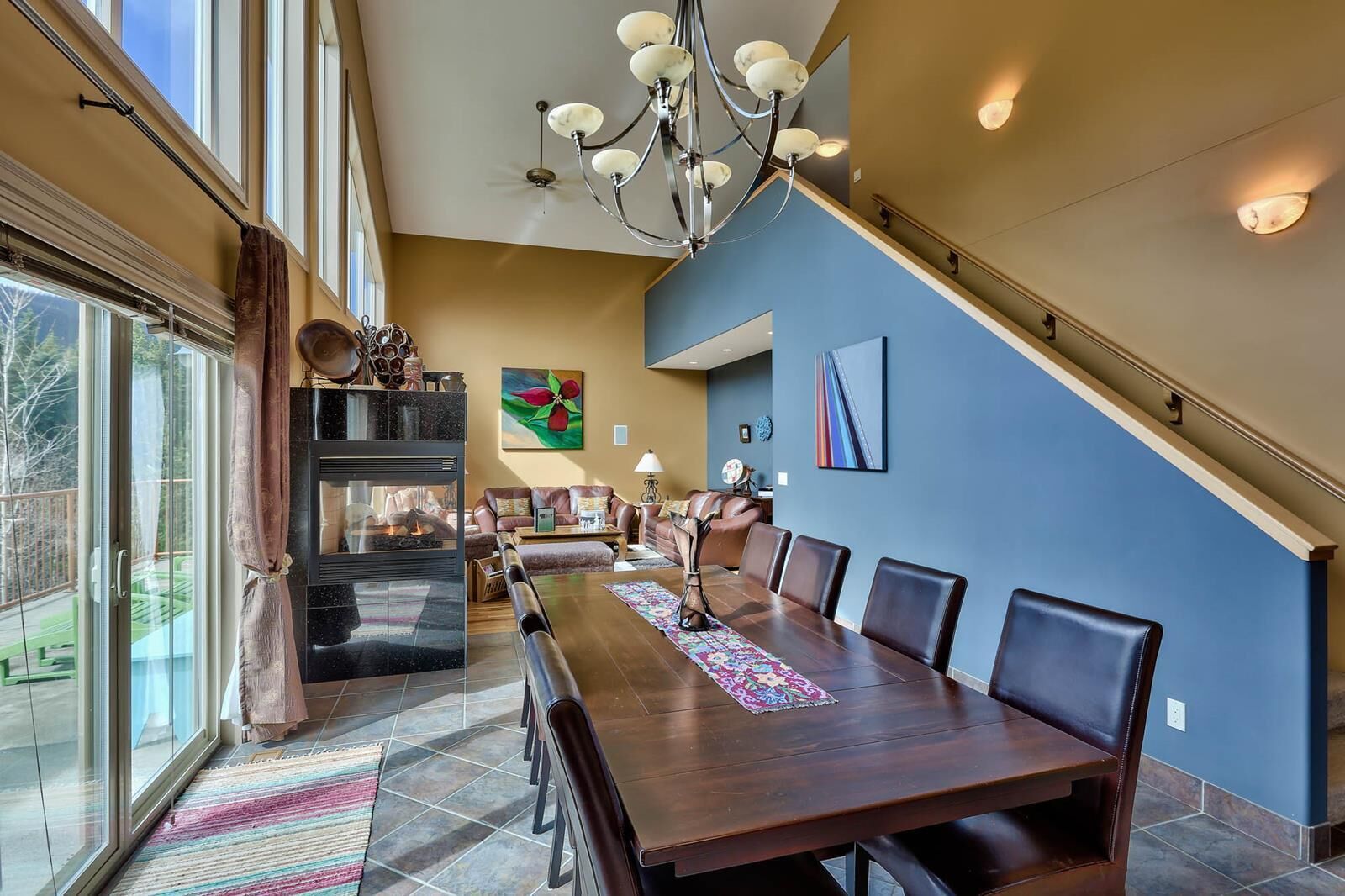 A spacious dining area with a long wooden table and chairs, a fireplace, and a staircase leading to an upper level.