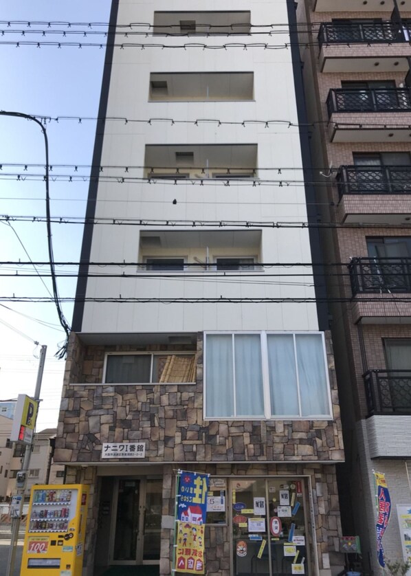 A multi-story building with a stone facade and large windows. There are visible signs and posters on the windows and doors. - Naniwa Tsutenkaku Hotel (Osaka)