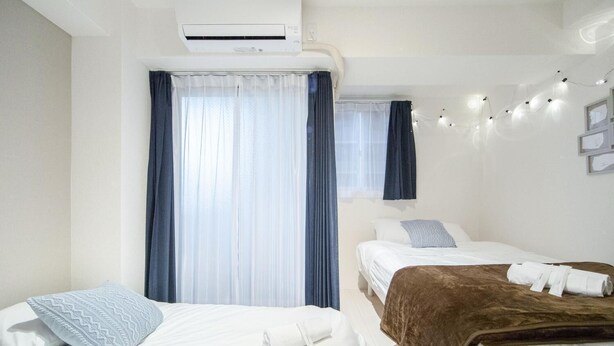 Ein Hotelzimmer mit zwei Betten, einem großen Fenster mit Vorhängen, einer Klimaanlage und einer Wandleuchte mit Lichterkette.