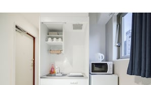 Eine kompakte Küchenzeile mit Mikrowelle, kleinem Kühlschrank, Spüle und einem Fenster mit Vorhängen.