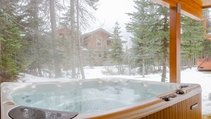 Un bain à remous dans un chalet en bois, avec un paysage enneigé et des arbres en arrière-plan.
