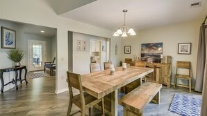 A spacious dining area with a wooden table and benches, a chandelier, and framed artwork on the walls. - Sunset Rentals | Rum Row 29 (Hilton Head Island)