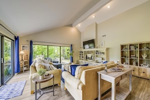 A spacious living area with a large window, a fireplace, and a wooden cabinet with decorative items. - Sunset Rentals | Rum Row 29 (Hilton Head Island)