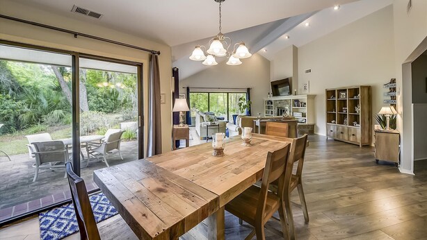 A spacious kitchen with a wooden dining table, built-in cabinets, and a large window overlooking a garden. - Sunset Rentals | Rum Row 29 (Hilton Head Island)