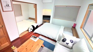 A small, well-lit room with a bed, a sofa, a wooden coffee table, and a TV. - Panda Stay Okayama (Okayama)