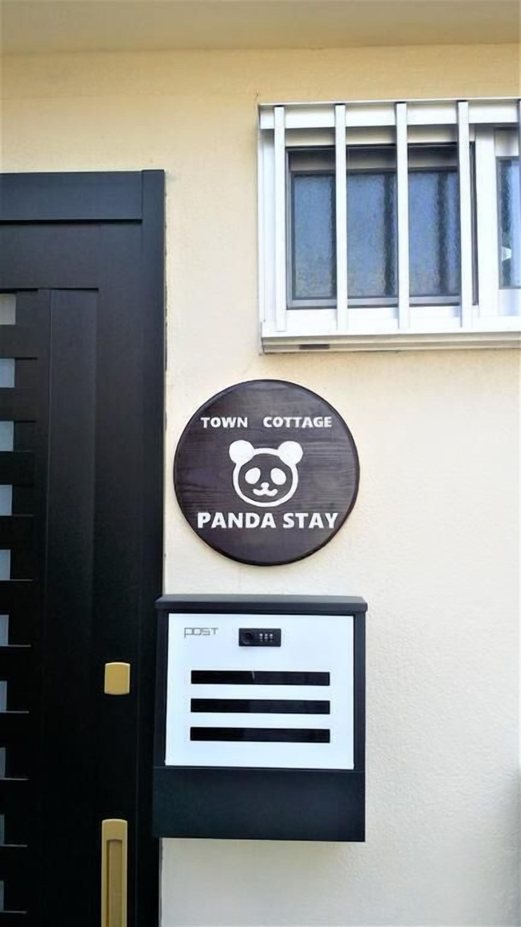 A black door with a window above it, a sign that reads "Town Cottage Panda Stay," and a mail slot with a label "POST."