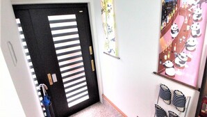 A hallway with a black door with horizontal stripes, a wall with a panda-themed poster, and a panda-themed rug. - Panda Stay Okayama (Okayama)