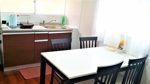 A compact kitchen with a white countertop, a sink, and a stove. There are two black chairs around a white table. - Panda Stay Okayama (Okayama)