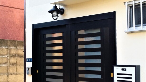 A black double door with horizontal slats, a small mailbox, and a security camera above the door. - Panda Stay Okayama (Okayama)