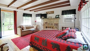 A bedroom with a large bed, a stone fireplace, a sofa, and a television.