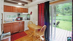 A kitchen with wooden cabinets, a stove, and a dining table with chairs. There is a sliding glass door leading to a deck with chairs.