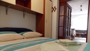 Un dormitorio con cama, almohadas y toallas dobladas. Hay una puerta que da a un espacio al aire libre.