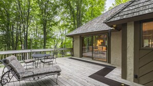 Eine Holzterrasse mit Gartenmöbeln, eine Glastür zu einem Innenbereich und Blick auf eine bewaldete Landschaft.
