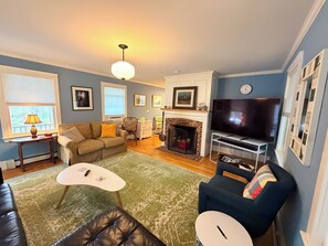 A living room with a fireplace, a television, a sofa, and a coffee table. - The Round Pond Getaway. Screened Porch · Fire Pit · Walk to Harbor (Bristol)