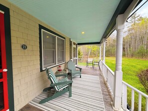 A covered porch with two rocking chairs, a small table, and a view of a green lawn and trees.