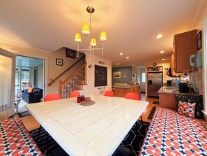 A modern kitchen with a central island, a dining area with a large table, and a staircase leading to another level. - The Round Pond Getaway. Screened Porch · Fire Pit · Walk to Harbor (Bristol)