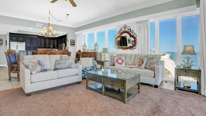 A spacious living room with a large window overlooking a beach, a chandelier, and a ceiling fan. - Phoenix Orange Beach 2006 by Liquid Life (Orange Beach)