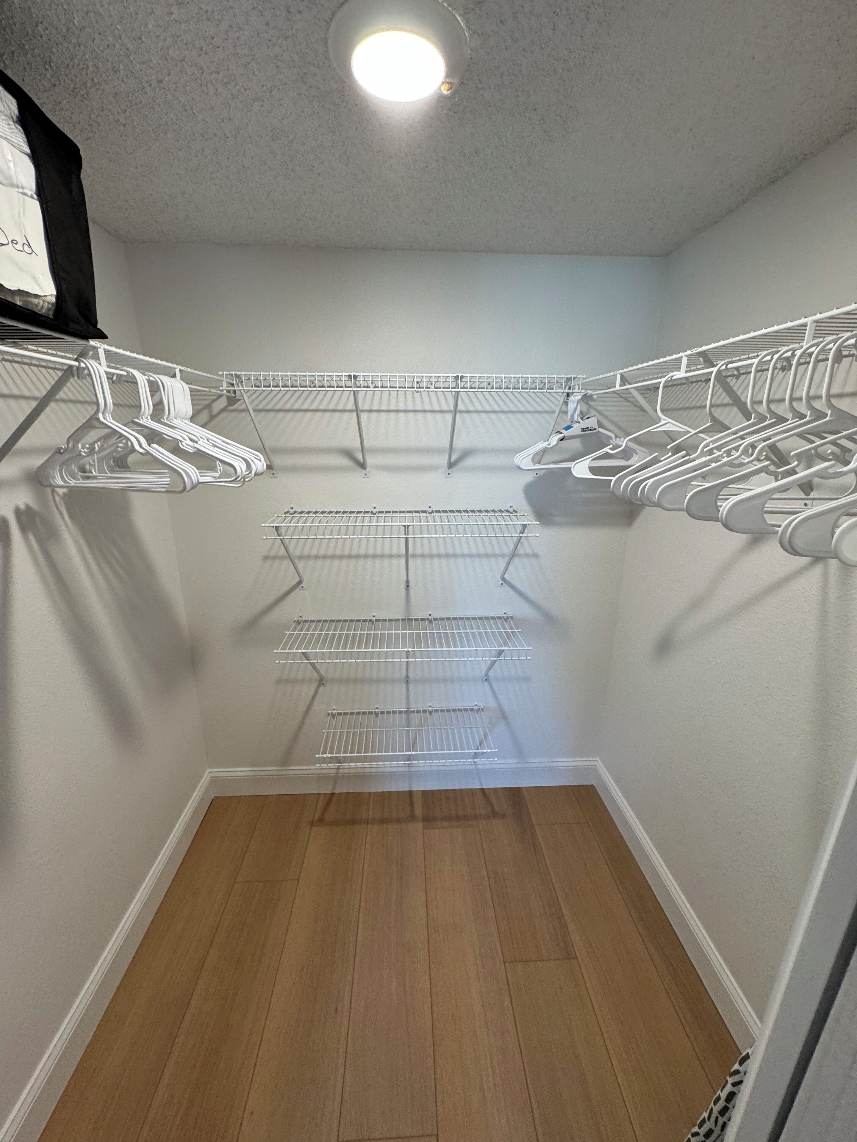 A walk-in closet with multiple shelves and hanging spaces, wooden flooring, and a ceiling light.