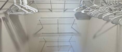 A walk-in closet with multiple shelves and hanging spaces, wooden flooring, and a ceiling light.