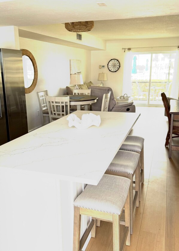 A spacious kitchen with a long white countertop, wooden stools, and a dining table. - Poolside Oasis at the Inlet, First Floor (Siesta Key)