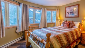 A bedroom with a wooden bed, a nightstand, a lamp, and a framed picture on the wall. - Ground floor 1 bedroom condo, great location close to village centre and next to ski runs (Sun Peaks)