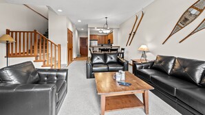 A modern living room with a sofa, coffee table, and a staircase. - Exceptional multi level 2 bedroom +den townhouse with easy access to nearby runs and lift (Sun Peaks)