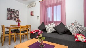 A living room with a sofa, a dining table with chairs, a vase with flowers, and a wall with a framed collage. - Apartment in Njivice with Seaview, Balcony, Air condition, WIFI (4687-1) (Njivice)