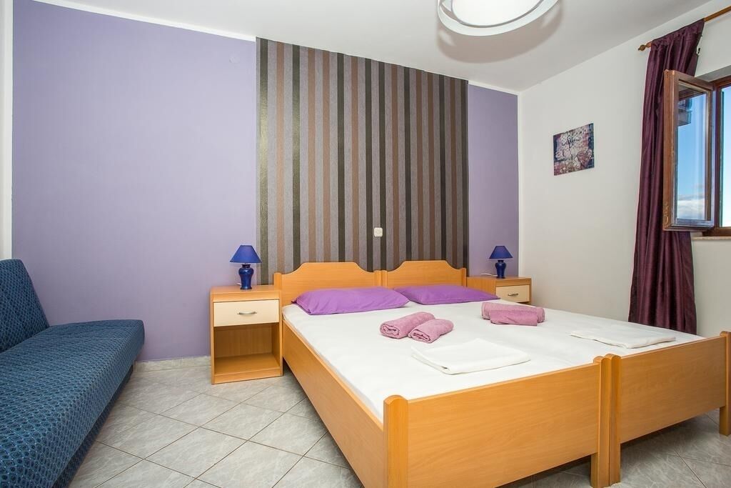Une chambre à coucher avec un lit en bois, deux tables de chevet, une commode, un canapé bleu et une fenêtre avec des rideaux.