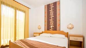 A bedroom with a wooden bed, a large window with curtains, a wall-mounted lamp, and a bedside table. - Apartment in Njivice with Seaview, Balcony, Air condition, WIFI (4687-1) (Njivice)