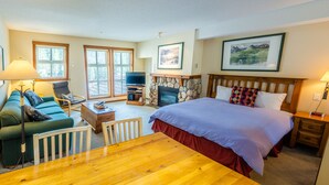 A hotel room with a bed, a TV, a fireplace, a sofa, and a dining table.