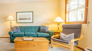 A living room with a green sofa, a wooden coffee table, a grey armchair, and two floor lamps.