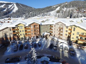 Une station de ski enneigée, avec des bâtiments à plusieurs étages, un parking et un paysage montagneux en toile de fond.