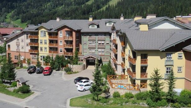 Un hotel de varios pisos con balcones, un estacionamiento y montañas al fondo.