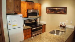 Una cocina con armarios de madera, microondas de acero inoxidable, horno empotrado, encimera de granito y un lavamanos.