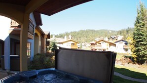 A hot tub with a wooden exterior, set on a patio with a view of a residential area and mountains in the background.