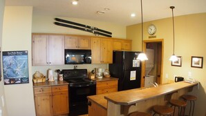 A kitchen with wooden cabinets, a black refrigerator, a stove, and a bar area with stools.
