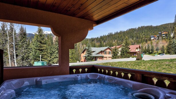 Una vasca idromassaggio con un pontile in legno e vista su una montagna e delle case.